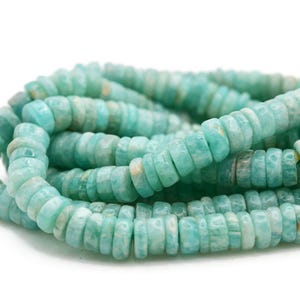 May include: Strands of Amazonite gemstone beads. The beads are a light turquoise color with a flat, disc shape. The beads are strung together, creating a coiled pattern against a white background. The Amazonite beads are a popular choice for jewelry making.