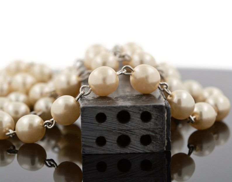 May include: A strand of faux pearl beads with a silver chain and a black rectangular object with holes in it.