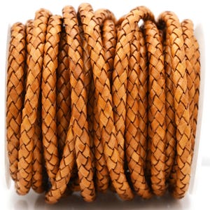 May include: A spool of braided leather cord in a warm, light brown color. The cord is tightly woven, creating a textured surface. The material appears to be genuine leather, suitable for crafting projects like jewelry making or leatherwork.