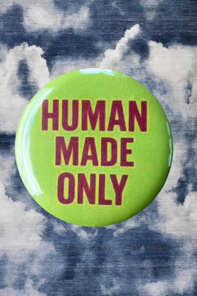 Pode incluir: Um bot&atilde;o redondo verde lim&atilde;o com o texto "HUMAN MADE ONLY" em letras bord&ocirc;. O bot&atilde;o est&aacute; sobre um fundo com um padr&atilde;o de nuvens azuis e brancas.