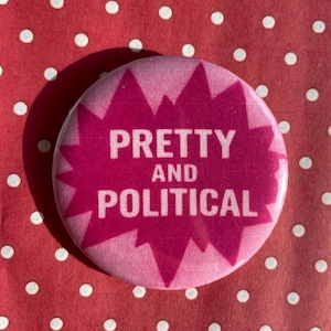 May include: A circular pink badge with the white text "PRETTY AND POLITICAL" set within a darker pink burst design. The badge is set against a red background with white polka dots.