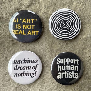 Pode incluir: Quatro botões redondos com texto. Um botão diz "AI 'ART' IS NOT REAL ART" em amarelo sobre preto. Outro tem um design de espiral em preto e branco. O terceiro diz "machines dream of nothing!" em preto sobre branco. O último diz "Support human artists" em branco sobre preto.