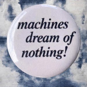 Pode incluir: Um bot&atilde;o branco com o texto "machines dream of nothing!" em preto, sobre um fundo nublado azul e branco. O bot&atilde;o &eacute; redondo e brilhante.
