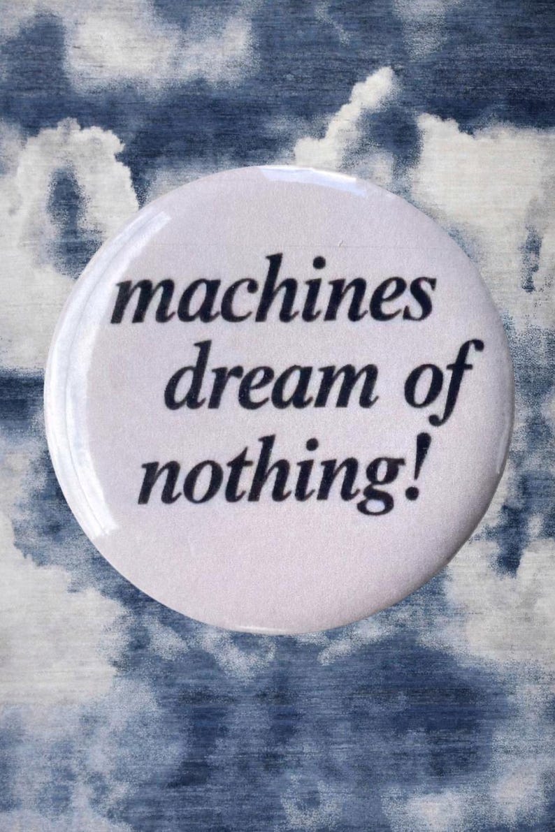 Pode incluir: Um bot&atilde;o branco com o texto "machines dream of nothing!" em preto, sobre um fundo nublado azul e branco. O bot&atilde;o &eacute; redondo e brilhante.