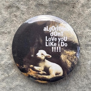 以下が含まれることがあります： 暗い背景に白い子羊が描かれた丸いボタン。「aLgOrIthMs dOnT Love yOU LiKe i Do !!!!」というテキストが白で印刷されています。