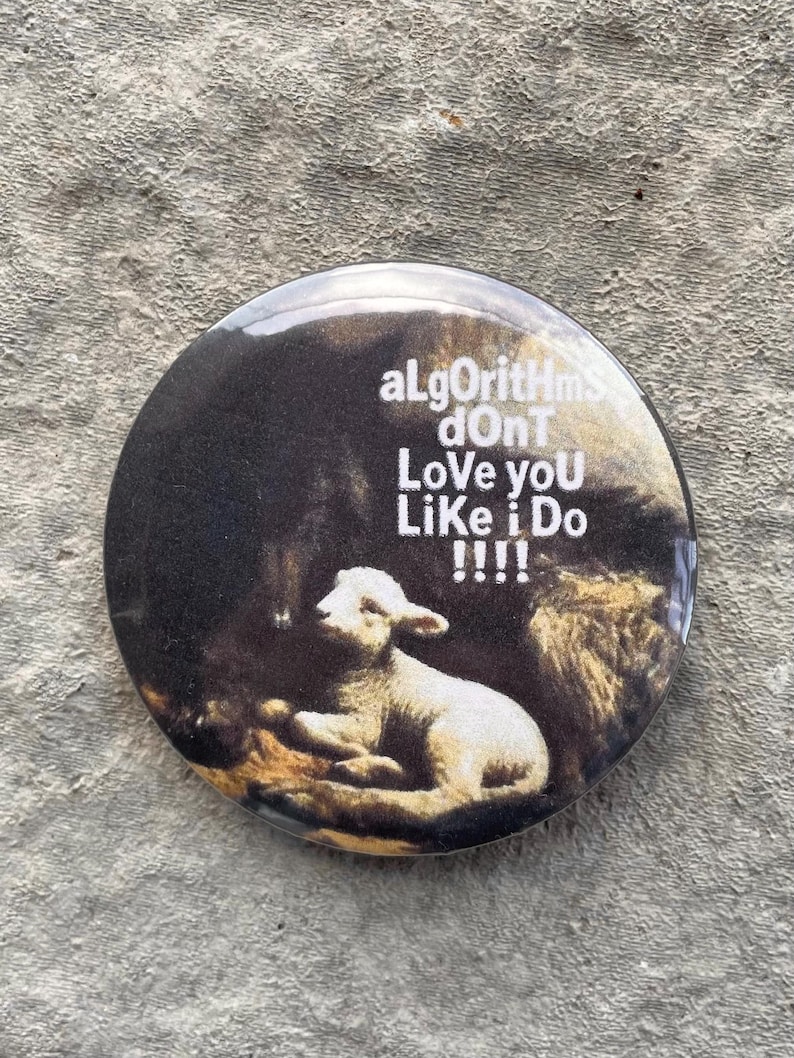 以下が含まれることがあります： 暗い背景に白い子羊が描かれた丸いボタン。「aLgOrIthMs dOnT Love yOU LiKe i Do !!!!」というテキストが白で印刷されています。