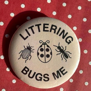 May include: A round, off-white button with the words "LITTERING BUGS ME" in black, surrounding illustrations of a beetle, ladybug, and ant. The button is set against a red background with white polka dots.