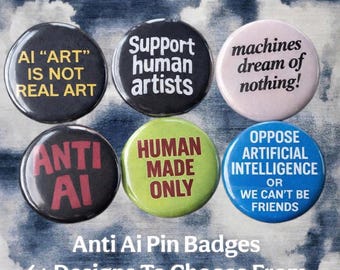 May include: Six circular pin badges with anti-AI slogans. The badges display phrases such as "AI 'ART' IS NOT REAL ART" and "Support human artists" in different colours. The background is a cloudy sky.