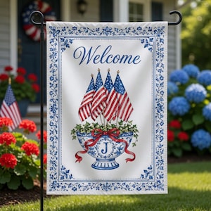 May include: A white garden flag with a blue floral border and the word "Welcome" in blue script. The flag features a blue and white decorative bowl with American flags and the letter "J".