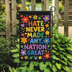 May include: A black garden flag with the text "HATE NEVER MADE ANY NATION GREAT" in colorful letters. The flag is decorated with various flowers and hearts in shades of red, yellow, orange, blue, and purple.