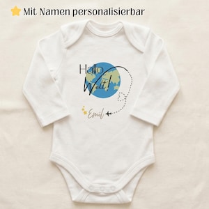 May include: A white long-sleeve baby bodysuit featuring a graphic of a blue and green globe with the text "Hallo Welt!" above it. A dashed flight path line with a small airplane icon circles the globe, ending near the name "Emil" and yellow stars.