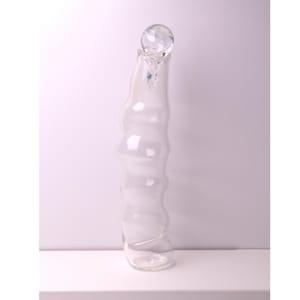 May include: A clear glass decorative bottle with a unique, wavy design. The bottle is topped with a crystal ball-shaped stopper. The bottle is tall and slender, with a rounded base.
