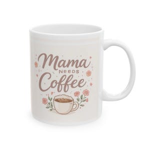 May include: White ceramic coffee mug with the text "Mama Needs Coffee" in a brown script font. The mug features a coffee cup illustration with floral accents, ideal for a coffee lover.