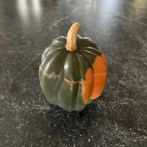 May include: A ceramic acorn squash figurine with a dark green body and an orange section. The squash has a light brown stem. The figurine is likely a decorative item for fall or Thanksgiving.