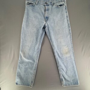 May include: Light blue denim jeans featuring a classic five-pocket design, a button and zipper fly closure, and belt loops at the waistband. The fabric displays a faded wash with subtle whiskering details and straight-cut legs throughout.