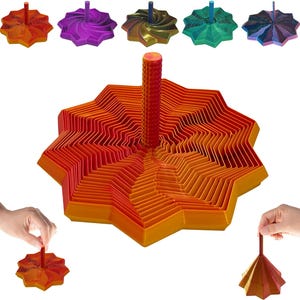 May include: A collection of colorful, star-shaped tops in various colors, including orange, purple, and green. Each top has a central post and a layered, geometric design. One is being held by a hand.