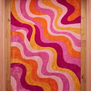May include: A rectangular area rug featuring a repeating pattern of vertical wavy lines in vibrant shades of hot pink, bright orange, light pink, and golden yellow. The rug has a plush, textured surface with distinct color-blocked sections.