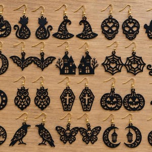 May include: A collection of black laser-cut acrylic earrings featuring various Halloween-themed designs including pumpkins, cats, skulls, ghosts, bats, haunted houses, spider webs, witches, owls, coffins, trees, ravens, butterflies, and lanterns with gold hooks.