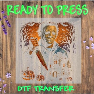 May include: A DTF transfer sheet featuring a graphic of a masked figure holding a knife, set against a background of bare trees, a house, and pumpkins. The text READY TO PRESS and DTF TRANSFER is printed in bright green at the top and bottom.