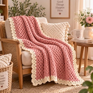 May include: A dusty rose crochet blanket with a cream-colored scalloped border draped over a wooden chair. The blanket features a classic granny square pattern with a textured stitch design, providing a soft and layered appearance across the seat.
