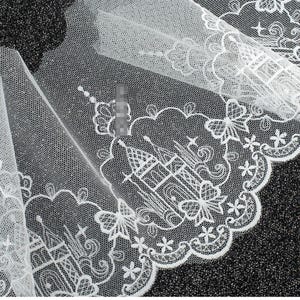 Peut inclure: Un tissu en tulle blanc avec une bordure en dentelle brod&eacute;e complexe. Le motif se compose de ch&acirc;teaux r&eacute;p&eacute;t&eacute;s entour&eacute;s de formes nuageuses, de petites &eacute;toiles et d'accents en forme de papillon le long d'un bord festonn&eacute; avec des d&eacute;tails floraux.