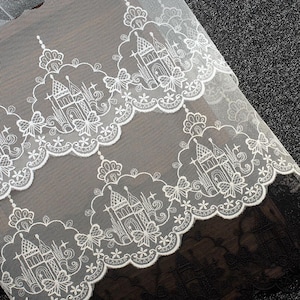 Peut inclure: Un tissu en dentelle blanche pr&eacute;sentant un motif r&eacute;p&eacute;titif de ch&acirc;teaux d&eacute;taill&eacute;s entour&eacute;s de bordures festonn&eacute;es. Le design complexe inclut de petites formes d'&eacute;toiles et des accents floraux, la dentelle blanche &eacute;tant superpos&eacute;e sur un fond sombre.