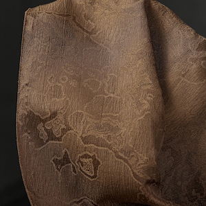 Könnte beinhalten: Nahaufnahme eines gefalteten braunen Stoffes mit einem dezenten Blumenmuster. Der Stoff hat eine strukturierte Oberfläche und einen warmen, erdigen Farbton. Die Falten erzeugen Schatten, die dem Bild Tiefe verleihen. Die Gesamtästhetik ist elegant und raffiniert.