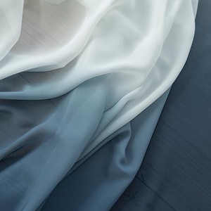 May include: A flowing fabric in shades of blue, transitioning from white to deep blue. The word "Blue" is displayed in red at the top left corner. The fabric appears soft and lightweight, with visible folds and a subtle sheen.