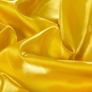 May include: Close-up of a vibrant yellow satin fabric. The fabric is draped and folded, creating shadows and highlights that emphasize its smooth, shiny texture. The folds and curves of the material add depth and visual interest.