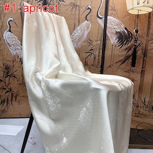 May include: A draped apricot-coloured fabric with a floral pattern, covering a chair. The fabric has a silky sheen, with the text "#1: apricot" in the upper left corner. The background features a decorative wall panel with crane illustrations.