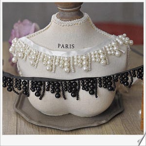 May include: A cream-colored mannequin bust displays two beaded trims. The top trim is white with pearl-like beads, and the bottom trim is black with black beads. The word "PARIS" is printed on the bust.