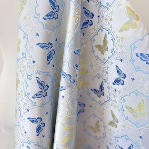 Peut inclure: Un tissu bleu clair avec un motif répétitif de papillons bleus et jaunes. Les papillons sont disposés sur un fond blanc avec un motif orné. Le tissu est drapé, révélant sa texture et son mouvement.