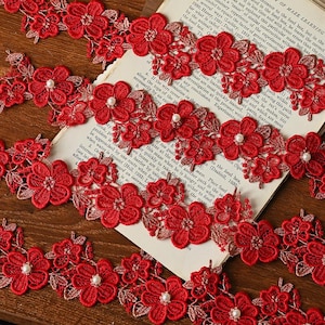 May include: Red lace trim featuring delicate floral patterns and pearl embellishments. This trim is ideal for adding a touch of elegance to any project.