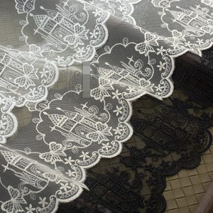 Peut inclure: Tissu en dentelle blanche pr&eacute;sentant un motif r&eacute;p&eacute;titif de ch&acirc;teaux brod&eacute;s &agrave; l'int&eacute;rieur de bordures festonn&eacute;es. Le design complexe comprend des accents floraux et un fond en maille fine. La dentelle est superpos&eacute;e sur un tissu noir assorti.