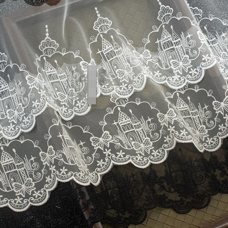 Peut inclure: Une bordure en dentelle blanche pr&eacute;sentant un motif r&eacute;p&eacute;titif de ch&acirc;teaux et de papillons brod&eacute;s avec des bords festonn&eacute;s. Le tissu en maille d&eacute;licat affiche des d&eacute;tails de broderie complexes dans un design continu pour la couture.