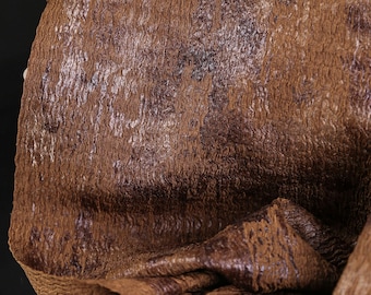 Puede incluir: Primer plano de una tela marrón texturizada con aspecto arrugado. El material tiene un patrón moteado con tonos marrón oscuro y púrpura. La tela está doblada, revelando su textura y brillo en capas.