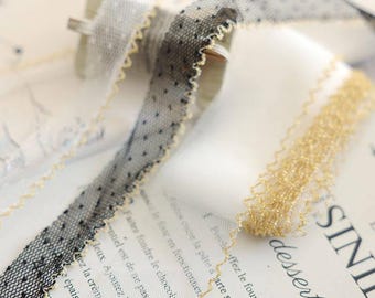 May include: A black dotted tulle ribbon with a gold scalloped edge and a separate gold metallic mesh ribbon. The black ribbon features a fine mesh texture with small dark dots and a shimmering gold trim along both sides of the fabric strip.