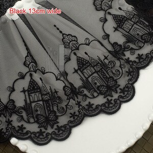 Peut inclure: Une bordure en dentelle noire pr&eacute;sentant un motif de ch&acirc;teau brod&eacute; r&eacute;p&eacute;titif avec des bords festonn&eacute;s. La dentelle poss&egrave;de un fond en maille fine et mesure 13 cm de large, comme indiqu&eacute; par le texte Black 13cm wide sur le tissu.