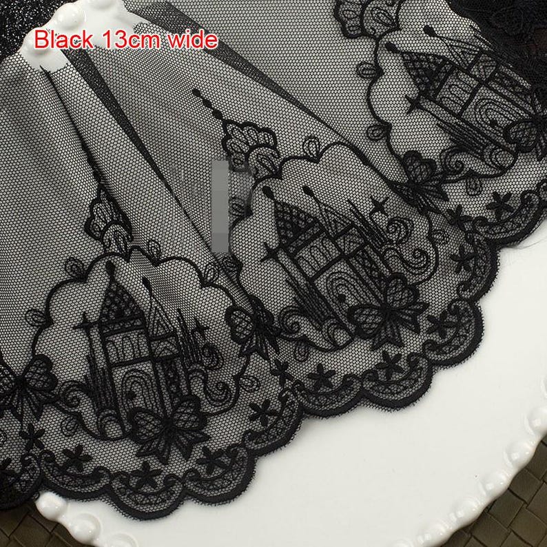 Peut inclure: Une bordure en dentelle noire pr&eacute;sentant un motif de ch&acirc;teau brod&eacute; r&eacute;p&eacute;titif avec des bords festonn&eacute;s. La dentelle poss&egrave;de un fond en maille fine et mesure 13 cm de large, comme indiqu&eacute; par le texte Black 13cm wide sur le tissu.