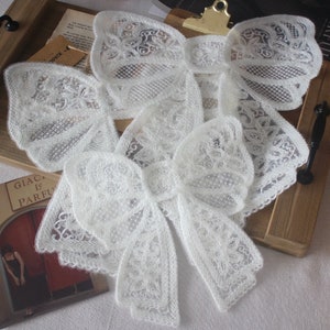 Puede incluir: Dos cuellos de encaje blanco con intrincados diseños florales. Los cuellos están hechos de un tejido delicado y transparente, perfectos para añadir un toque de elegancia a cualquier atuendo.