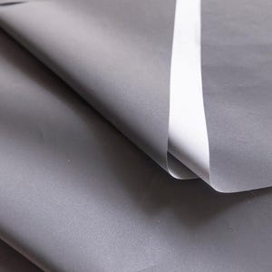 Puede incluir: Primer plano de una tela gris con una franja blanca que recorre el centro. La tela está doblada sobre sí misma, creando un efecto de capas.