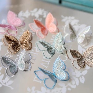 May include: Assortment of embroidered butterfly appliques in various colors, including pink, brown, blue, and silver. The butterflies are delicate and intricate, with a sheer fabric overlay.