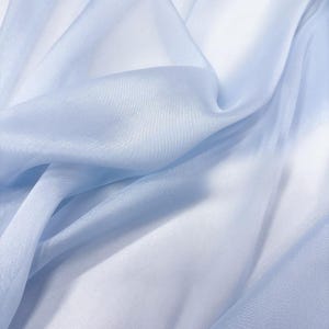 May include: A close-up shot of a light blue sheer fabric with soft folds and a delicate texture. The fabric appears to be lightweight and flowing, with subtle variations in color and highlights.
