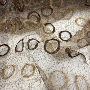 May include: A sheer, lightweight fabric featuring a delicate, web-like mesh pattern in dark brown. The material is adorned with embroidered circular motifs in alternating shades of metallic gold and dark brown, creating a layered, textured appearance.