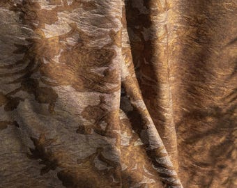 Puede incluir: Primer plano de una tela texturizada con un estampado floral. La tela tiene un brillo metálico con tonos marrones y dorados. El diseño floral es de un tono marrón más oscuro, creando un contraste con el fondo más claro.