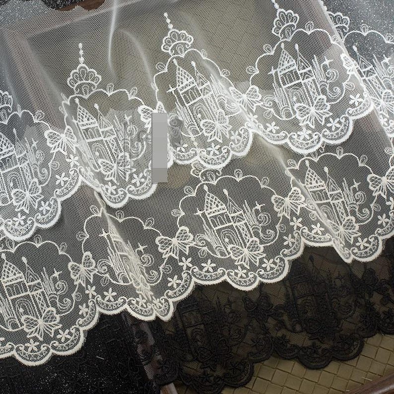 Peut inclure: Une bordure en dentelle blanche pr&eacute;sentant un motif r&eacute;p&eacute;titif de ch&acirc;teaux et de papillons brod&eacute;s avec un bord festonn&eacute;. Le design complexe est cousu sur un tissu en maille transparente, mettant en valeur des motifs architecturaux d&eacute;taill&eacute;s.