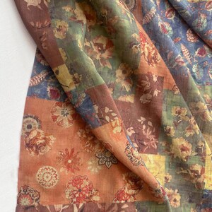 May include: A patchwork textile featuring a floral pattern in shades of orange, brown, green, and blue. The design incorporates various floral motifs and geometric shapes, creating a vintage aesthetic. The fabric appears to be lightweight and flowing.