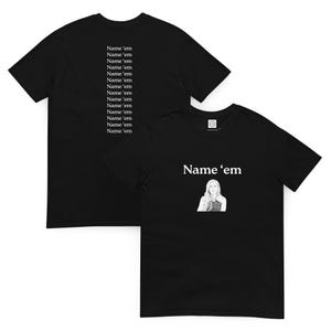 Puede incluir: Dos camisetas negras. Una presenta el texto "Name 'em" y un gráfico de una mujer. La otra tiene el mismo texto repetido en la espalda. El texto es blanco.