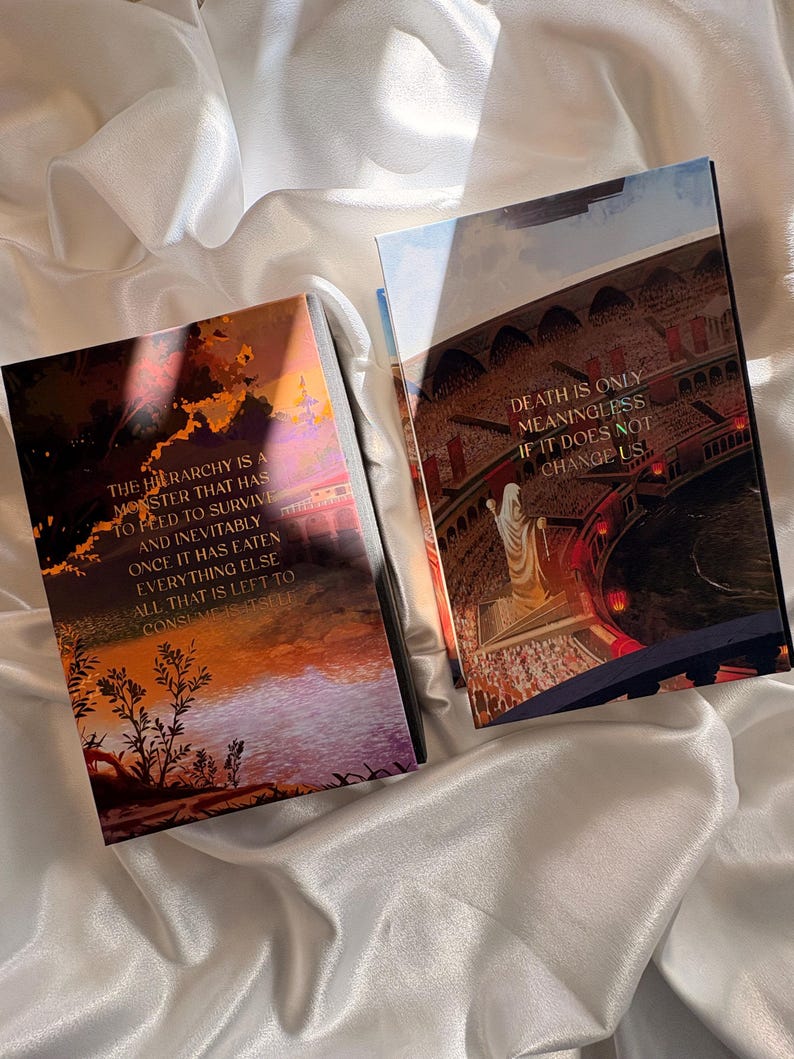 May include: Two hardcover books with fantasy art covers. One features a sunset scene with text: "THE HIERARCHY IS A MONSTER THAT HAS TO FEED TO SURVIVE." The other book shows a crowd scene with text: "DEATH IS ONLY MEANINGLESS IF IT DOES NOT CHANGE US."