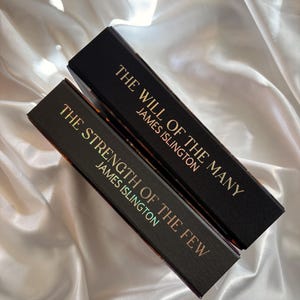 May include: Two hardcover books with black covers and gold lettering. The top book reads "THE WILL OF THE MANY" and "JAMES ISLINGTON." The bottom book reads "THE STRENGTH OF THE FEW" and "JAMES ISLINGTON."